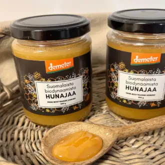 kaksi hunajapurkkia, rottinkitarjotin, puulusikka jossa on hunajaa, suomalainen biodynaaminen hunaja, demeter, puhdas hunaja