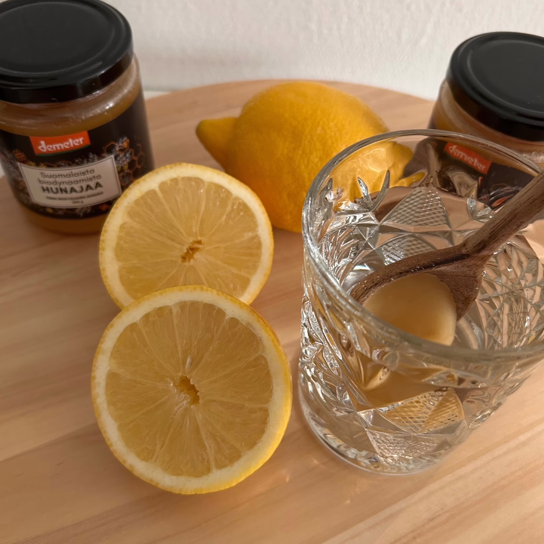 Sitruunan palat pöydällä sekä biodynaamista hujanaa, vieressä lasi jossa puisessa lusikassa hunajaa